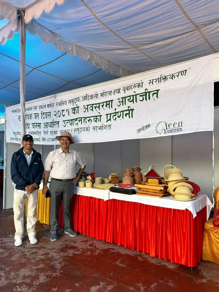 Two men beside an exhibition stall displaying locally made pottery and woven goods under a marquee.