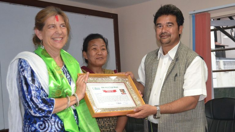 Three people holding a framed certificate of appreciation printed on Green Foundation Nepal letterhead.